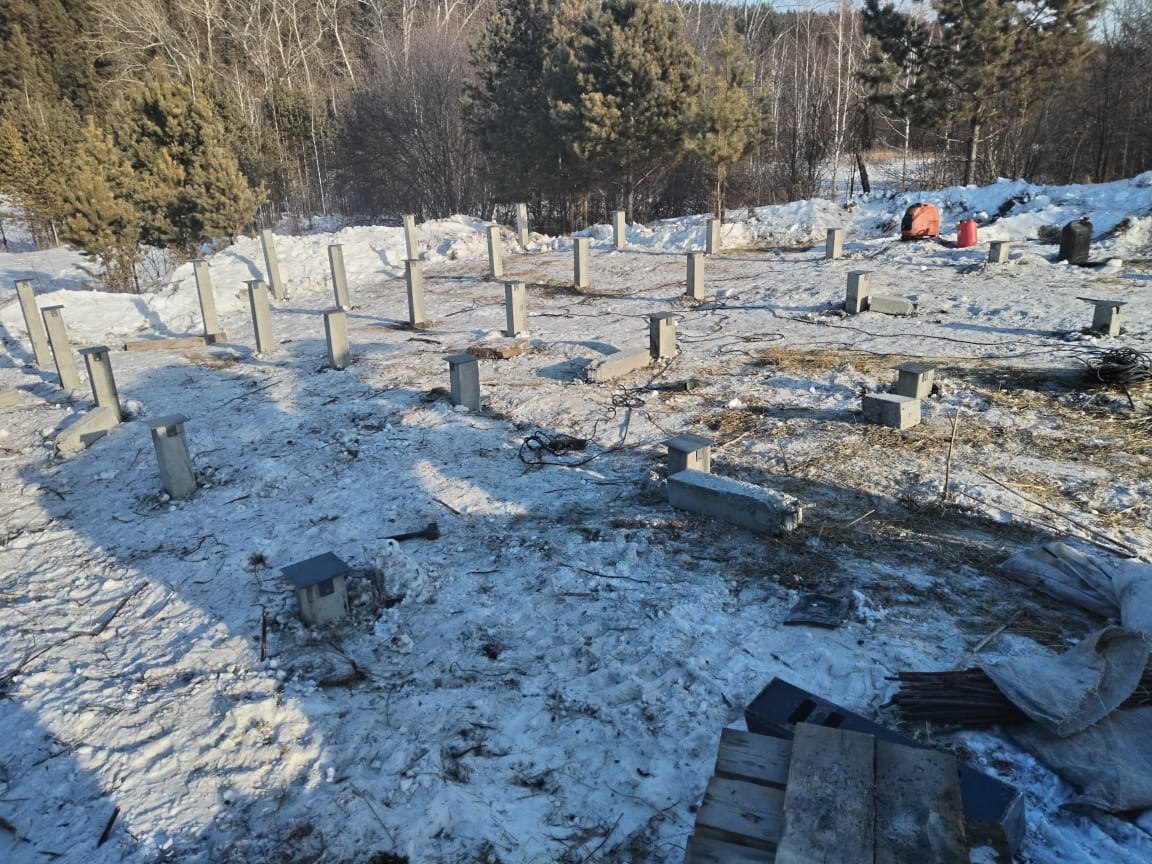 Строительная площадка зимой с установленными железобетонными сваями на снежном участке в окружении леса